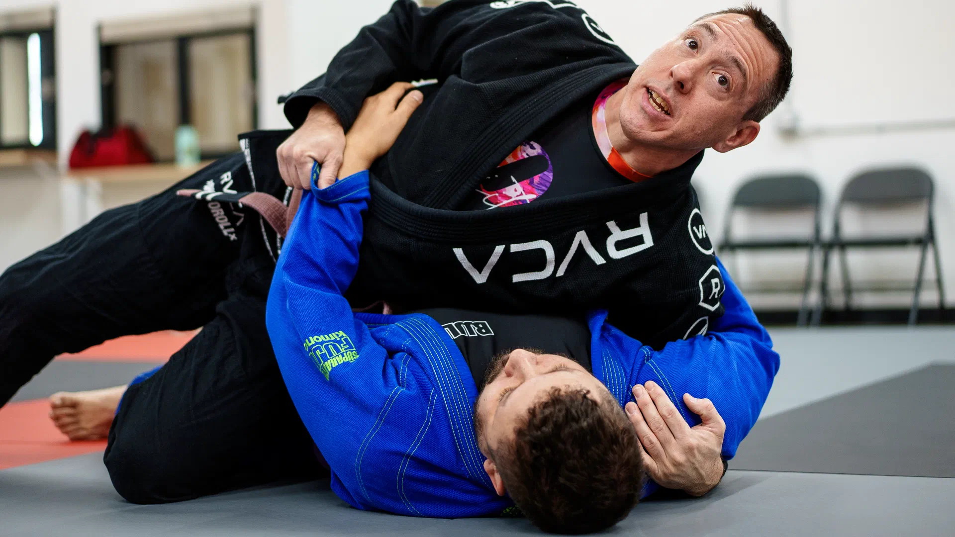 Brazilian Jiu-Jitsu coach demonstrating side-control technique with adult student at a Madison BJJ class.