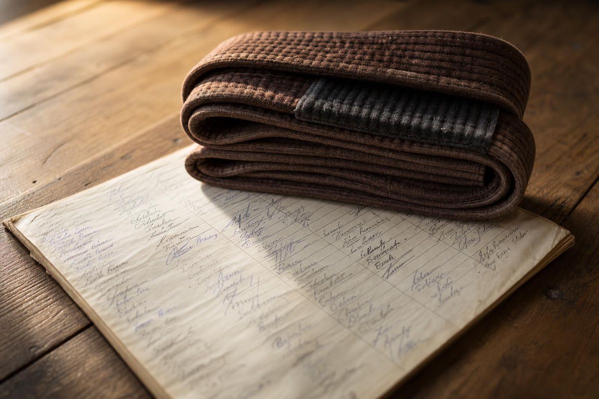 A brown BJJ belt folded on top of a well-worn attendance ledger or sign-in sheet, warm natural light