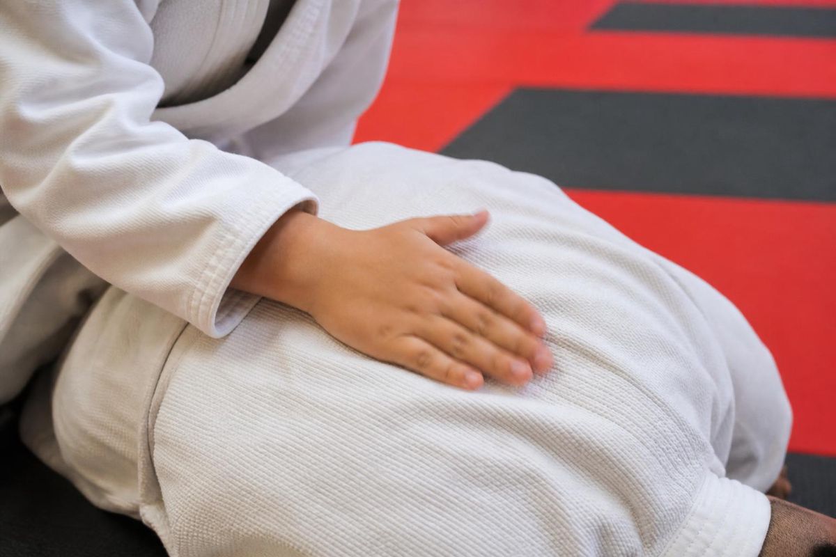 close-up of a kid's hand tapping firmly on a training partner's back to signal submission