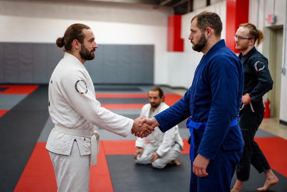 Two training partners shaking hands before a round in a Journey BJJ class, calm and matter-of-fact rather than confrontational