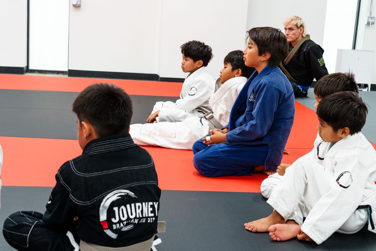 A group of kids in white gis seated attentively on the Journey BJJ mats