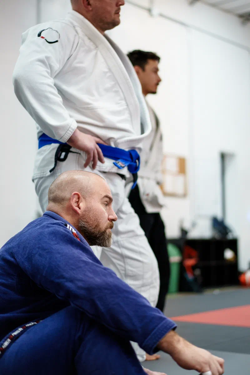 Happy adult BJJ students sitting on mats after class at Journey Academy Madison
