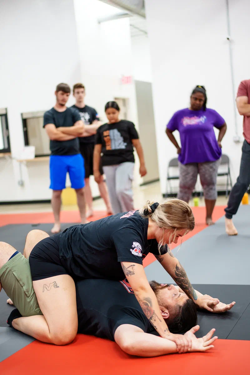 Journey BJJ coach demonstrating arm-pin defense with Madison self-defense student