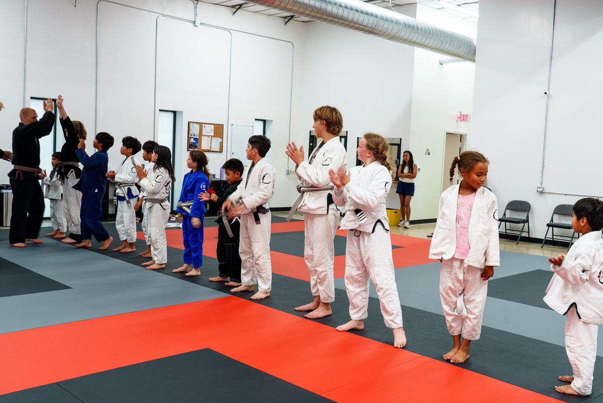 Wide shot of a kids' BJJ class lined up on the mat, one child at the end of the line looking away from the group