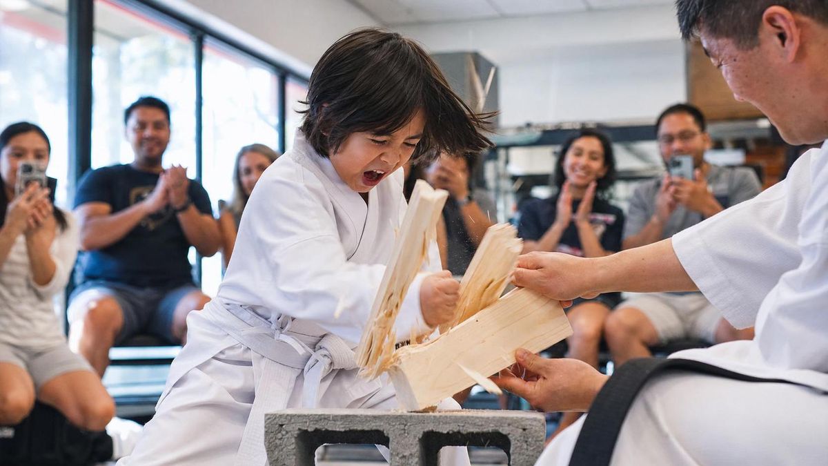 A child breaking a board at a karate demo while parents applaud
