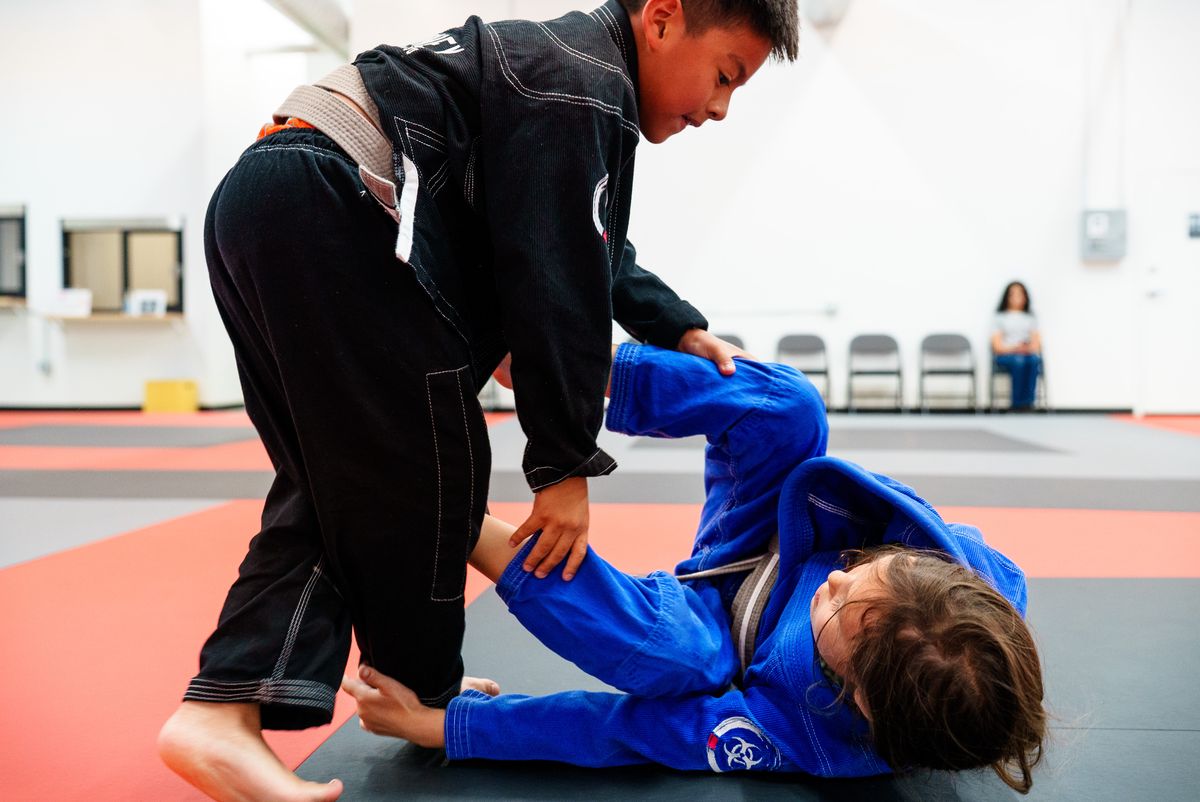 two kids in gis in a live scramble on the mat, one caught underneath and working to escape
